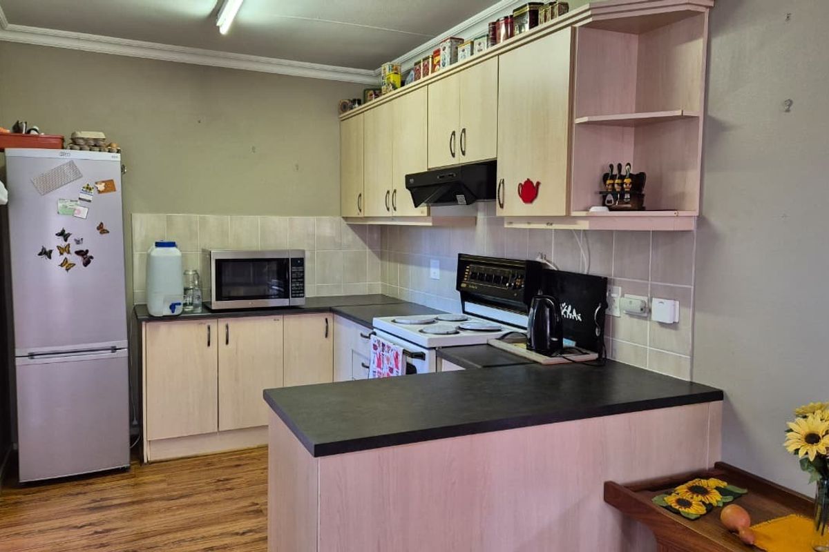 A functional kitchen featuring light-toned laminate cabinetry, dark countertops, a tiled backsplash, and an integrated electric stove with an extractor fan.