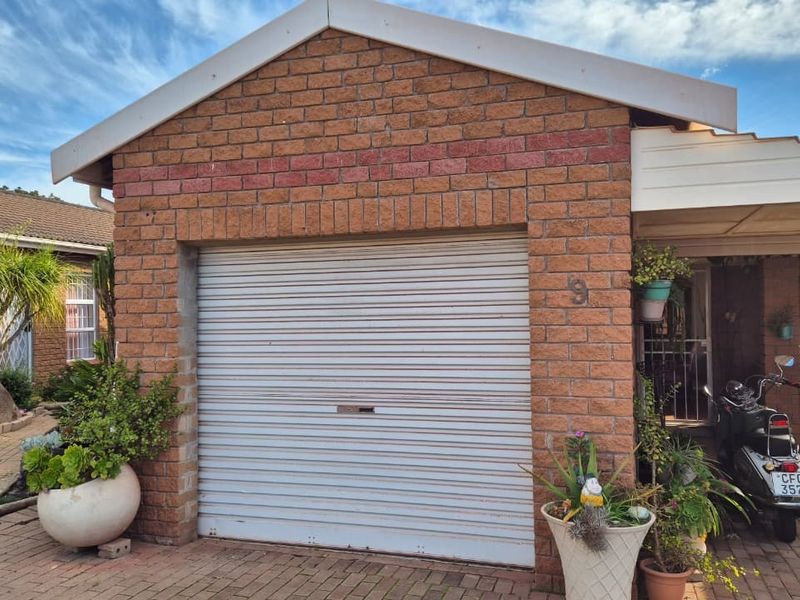 A residential garage featuring a roller shutter door and face brick exterior, situated within a retirement village setting with paved access.