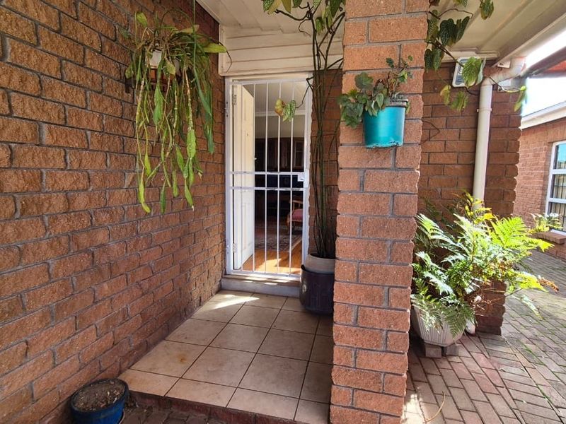 A covered brick patio entrance featuring tiled flooring and a security gate, providing access to the main living area.