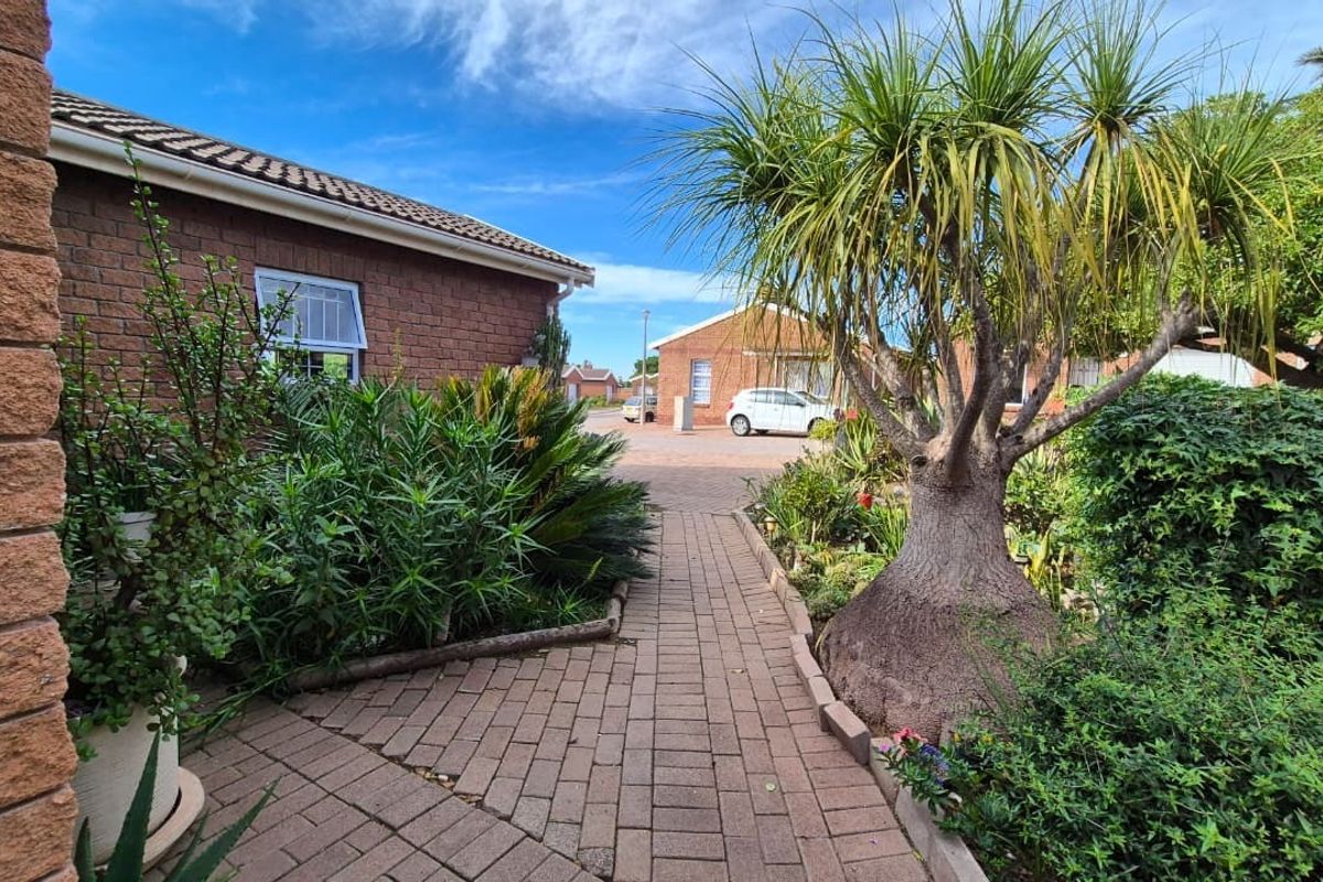 A well-maintained brick-paved pathway leads through a landscaped garden area alongside a brick residential building in a retirement village setting.