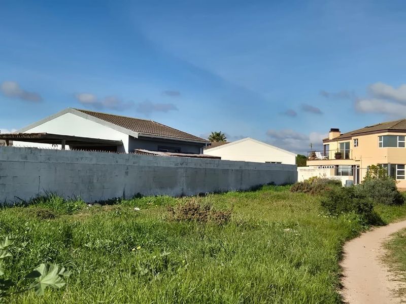 A vacant residential plot featuring a perimeter wall with security spikes, surrounded by established neighborhood housing.