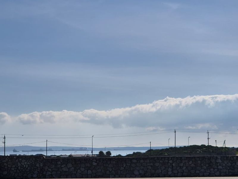 A scenic view overlooking the coastline and horizon, featuring a stone boundary wall in the foreground.