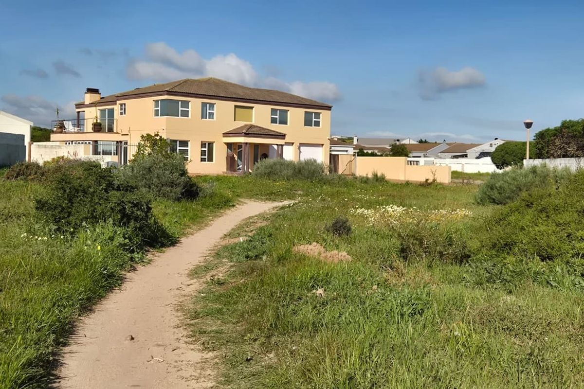 A view of a residential property from an adjacent vacant plot, showing the building facade, boundary walls, and surrounding natural vegetation.