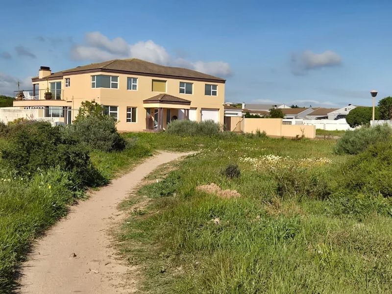 A view of a residential property from an adjacent vacant plot, showing the building facade, boundary walls, and surrounding natural vegetation.