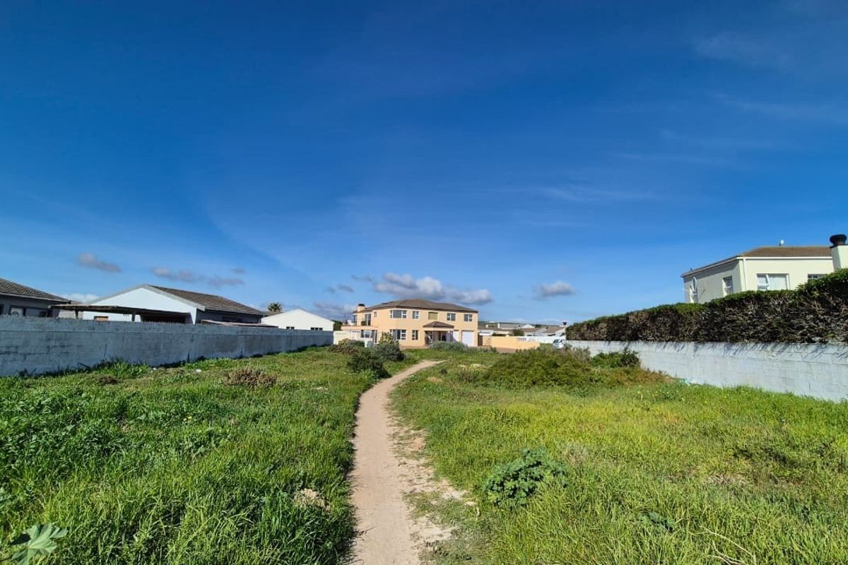 A vacant residential plot featuring boundary walls and a central pathway, surrounded by established neighborhood housing.