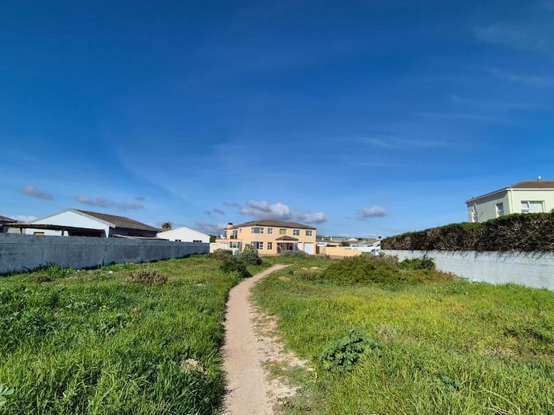 A vacant residential plot featuring boundary walls and a central pathway, surrounded by established neighborhood housing.