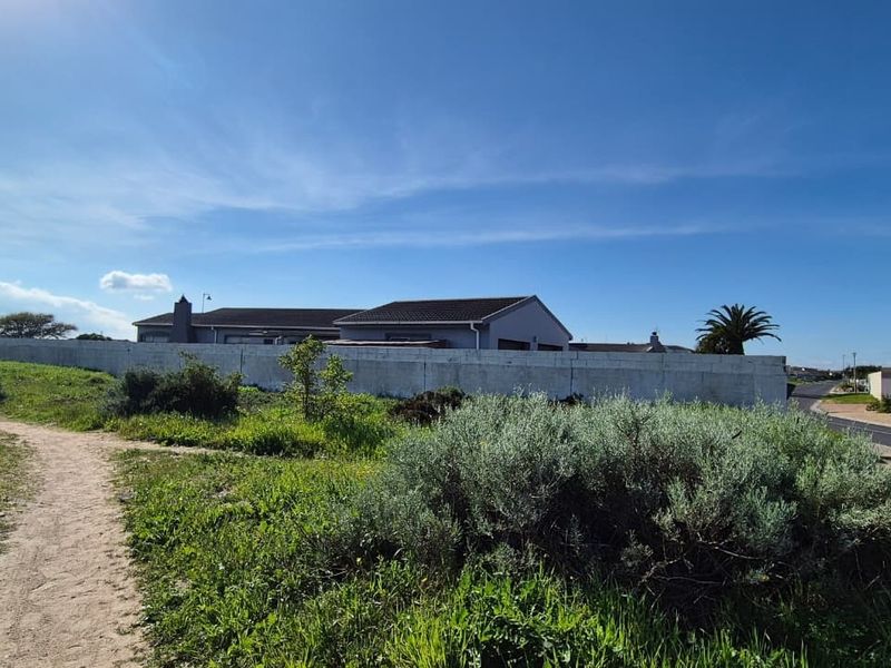 A view of the residential property from the adjacent vacant land, showing the perimeter wall and surrounding landscape.