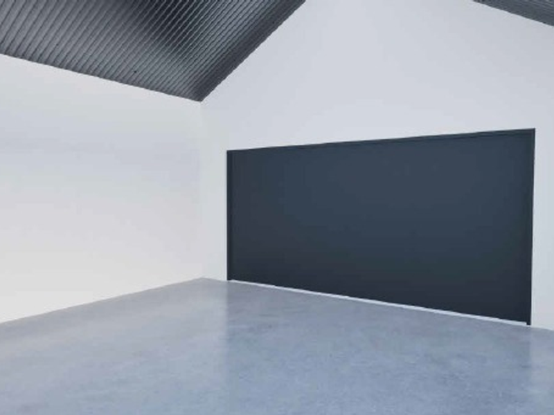 A clean, empty garage space featuring polished concrete flooring, white walls, and a high-pitched corrugated metal ceiling.