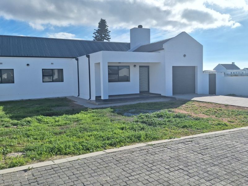 A modern single-story house featuring a white facade, corrugated metal roof, integrated garage, and a paved driveway with an unlandscaped front garden.