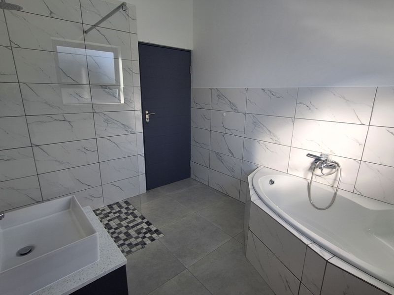 Modern bathroom featuring marble-look wall tiles, a built-in bathtub, a vessel sink vanity, and a walk-in shower area.