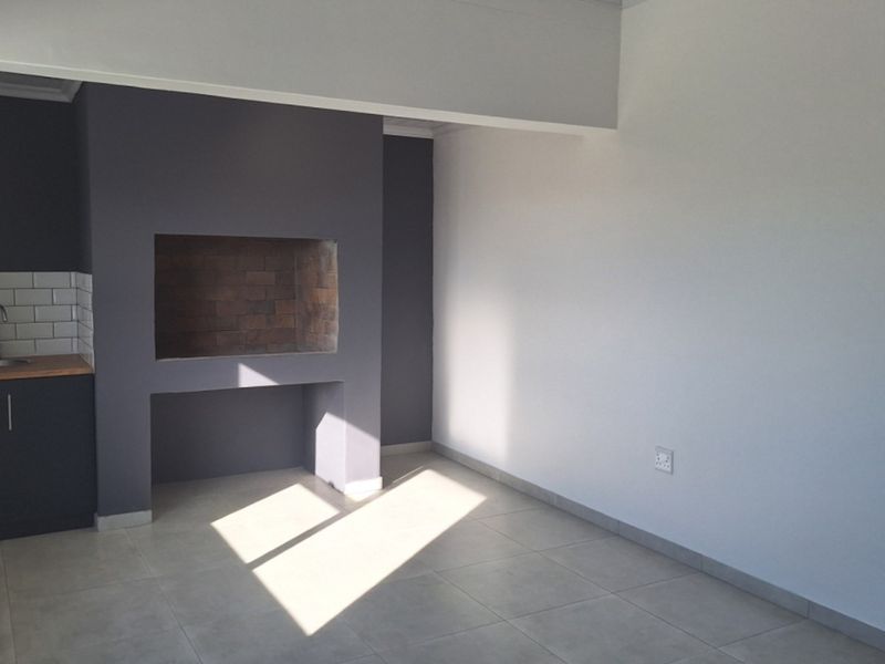 An open-plan living area featuring a built-in fireplace, tiled flooring, and a compact kitchenette corner with a sink and subway tile backsplash.