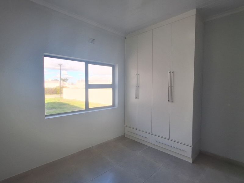 A bright, empty bedroom featuring neutral tiled flooring, clean white walls, and modern built-in cupboards with ample storage space.