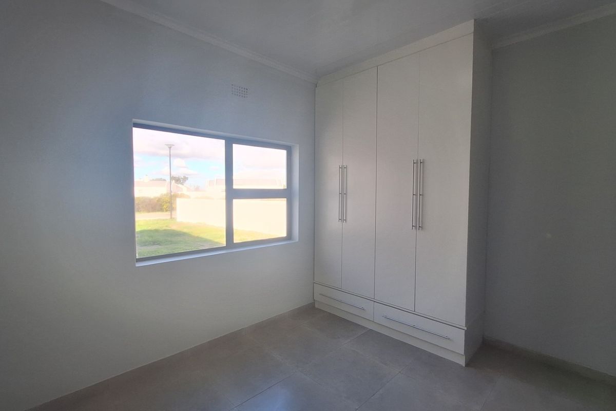 A bright, empty bedroom featuring neutral tiled flooring, clean white walls, and modern built-in cupboards with ample storage space.