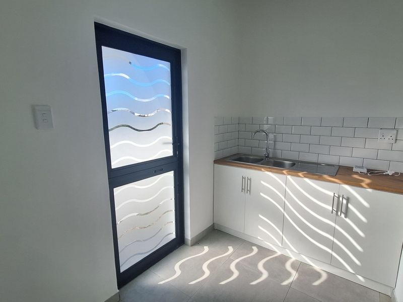 A clean and modern scullery area featuring a stainless steel sink, subway tile backsplash, and white cabinetry with a wood-look countertop.