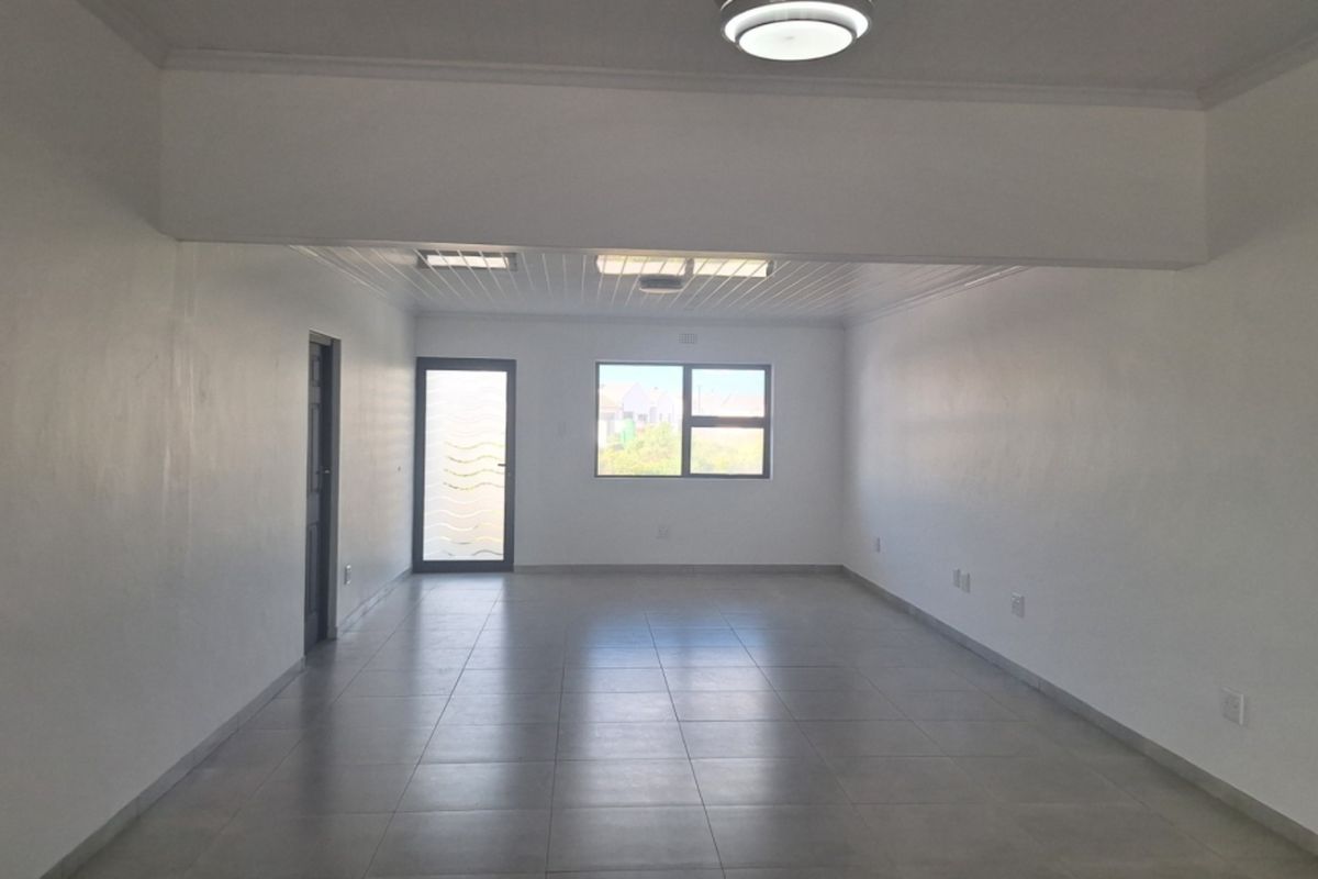 A spacious, empty living area featuring neutral tiled flooring, clean white walls, and natural light from the window and glass-paneled door.