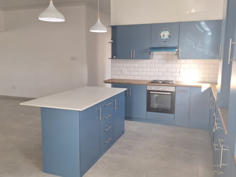 Modern kitchen featuring blue cabinetry, a central island with stone countertop, subway tile backsplash, and integrated appliances in an open-plan layout.