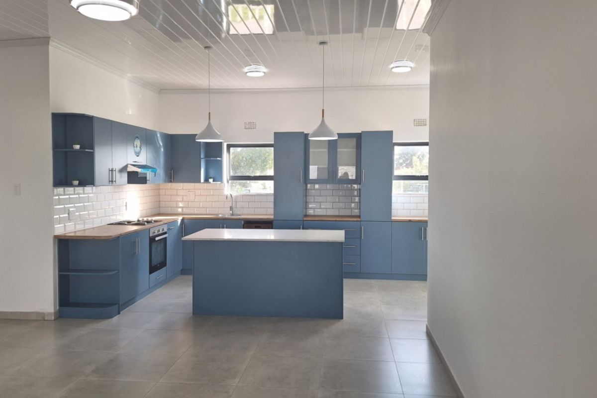 Modern kitchen featuring blue cabinetry, a central island, subway tile backsplash, built-in oven and hob, and tiled flooring.
