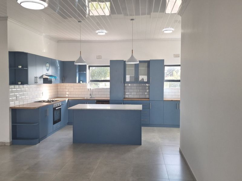 Modern kitchen featuring blue cabinetry, a central island, subway tile backsplash, built-in oven and hob, and tiled flooring.