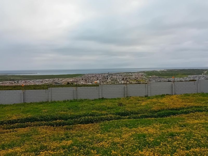 A wide-angle view of the surrounding landscape and coastline, featuring a concrete block boundary wall and security fencing in the foreground.