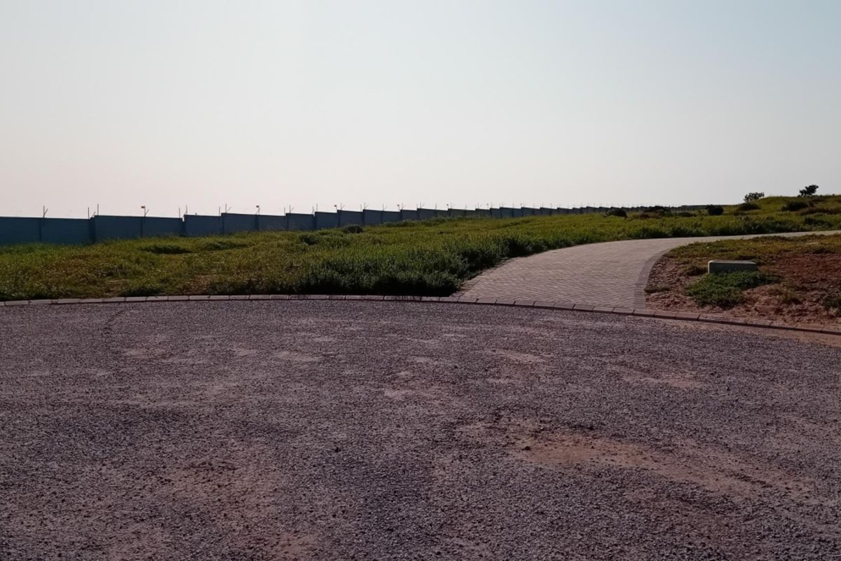 A view of a vacant residential plot featuring a gravel driveway, paved walkway, perimeter fencing, and an installed street light.