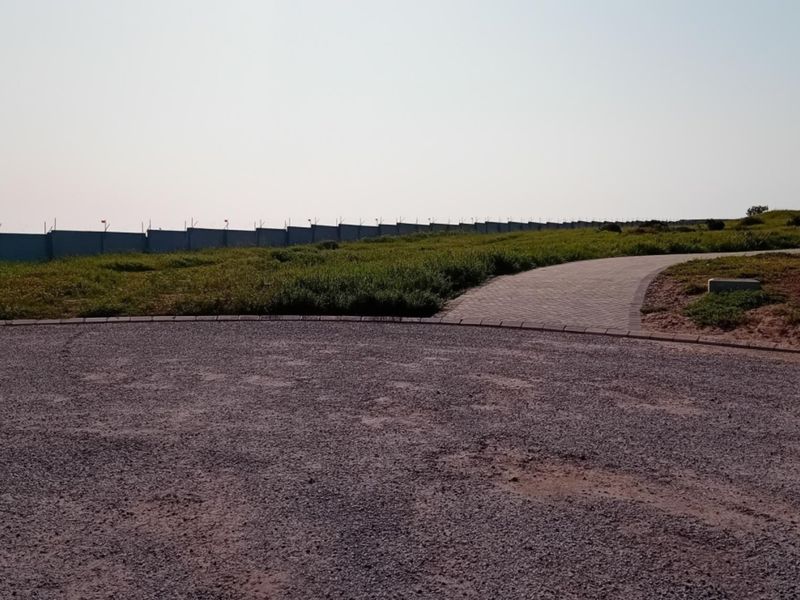 A view of a vacant residential plot featuring a gravel driveway, paved walkway, perimeter fencing, and an installed street light.