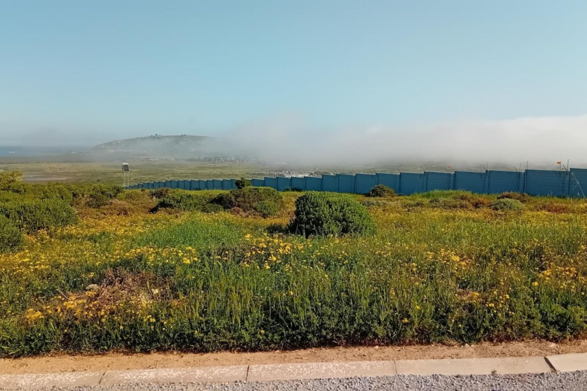 A scenic view of the vacant residential land featuring natural vegetation, perimeter fencing, and distant coastal landscape under a clear sky.