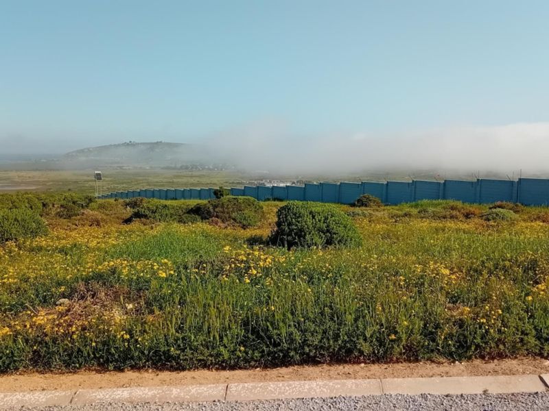 A scenic view of the vacant residential land featuring natural vegetation, perimeter fencing, and distant coastal landscape under a clear sky.