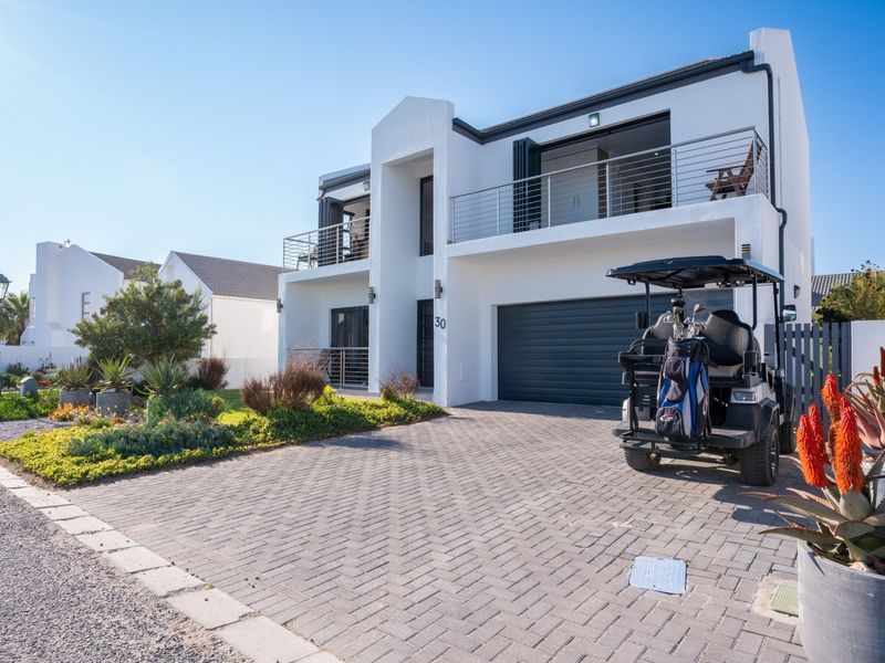 Modern double-story residential facade featuring a paved driveway, double garage, and upper-level balcony with stainless steel balustrades.