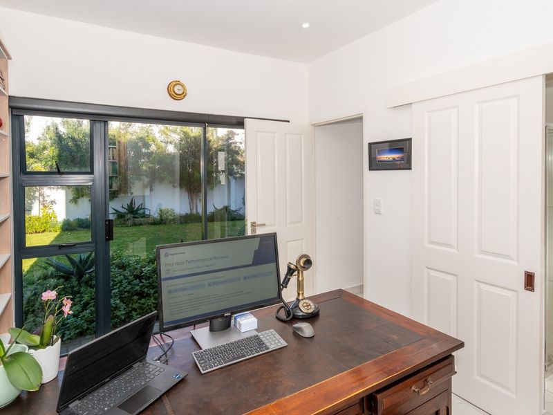 A functional home office featuring built-in shelving, large sliding glass doors providing garden access, and an adjoining bathroom with a shower.