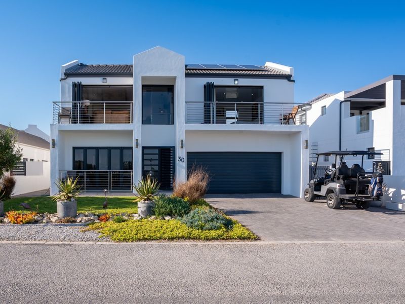 Modern two-story residential property featuring a double garage, upper-level balcony with metal railings, solar panels, and a well-maintained front garden and paved driveway.