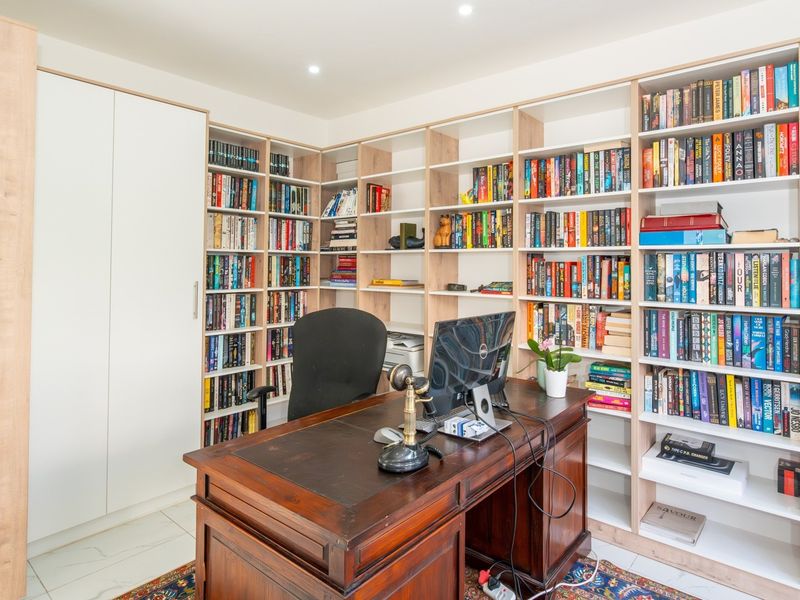 A well-appointed home office featuring extensive built-in floor-to-ceiling shelving and cabinetry, providing ample storage and a functional workspace.