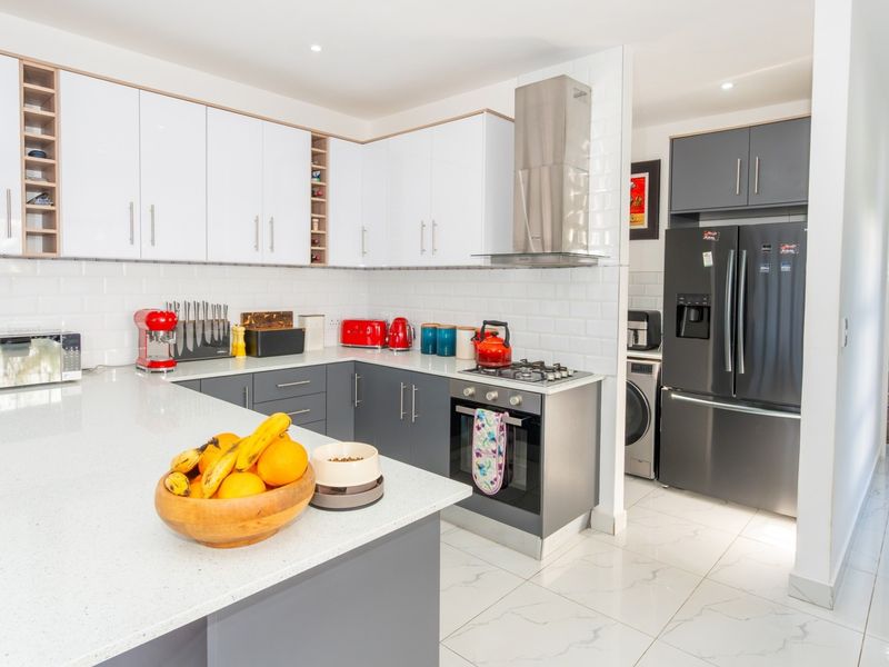 Modern kitchen featuring white gloss cabinetry, quartz countertops, subway tile backsplash, and high-quality stainless steel appliances with integrated gas hob and oven.