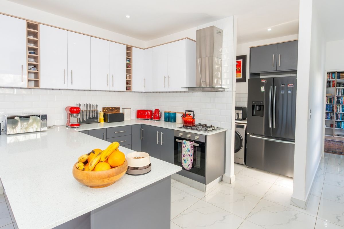 Modern kitchen featuring white gloss cabinetry, quartz countertops, subway tile backsplash, and high-quality stainless steel appliances with integrated gas hob and oven.