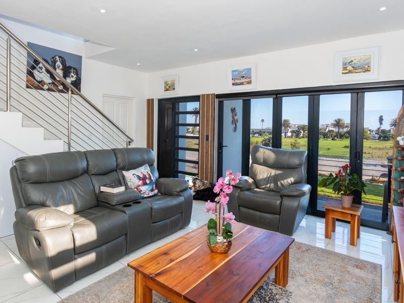 A bright, modern living room featuring tiled floors, a contemporary staircase with stainless steel railings, and large glass doors opening to an outdoor view.