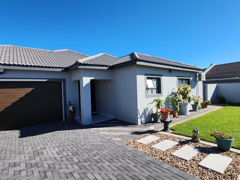 Front view of a modern single-story house featuring a paved driveway, integrated garage, and a well-maintained lawn with a stone pathway.