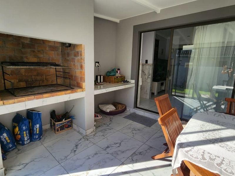 Covered patio area featuring a built-in brick braai, prep counter, and marble-look tiled flooring, with direct access to the interior via sliding glass doors.
