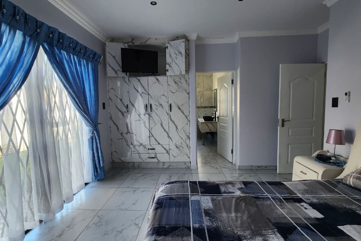 Spacious bedroom featuring marble-effect built-in cupboards, tiled flooring, and direct access to an en-suite bathroom through a standard door.