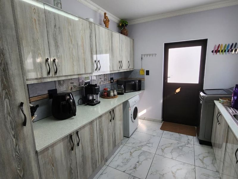 A functional laundry room featuring wood-look cabinetry, stone-effect tiled flooring, and a double basin sink with direct access to the exterior.