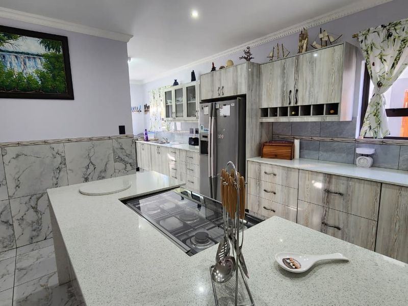 Spacious kitchen featuring a central island with a built-in hob, marble-effect wall tiles, ample fitted cabinetry, and modern quartz countertops.