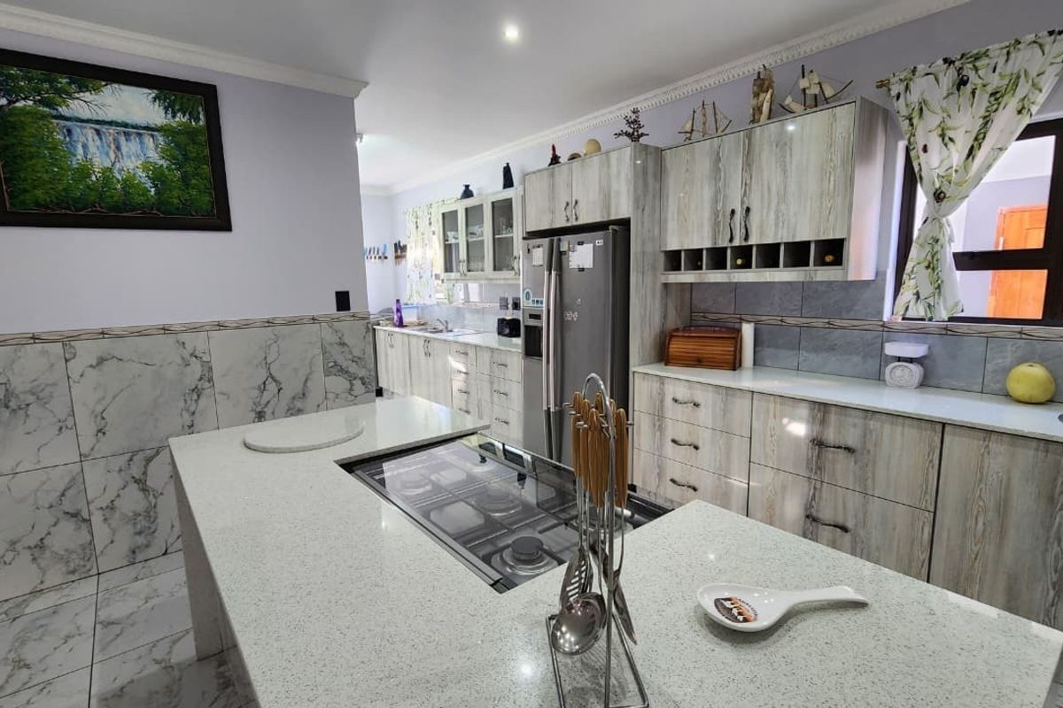 Spacious kitchen featuring a central island with a built-in hob, marble-effect wall tiles, ample fitted cabinetry, and modern quartz countertops.