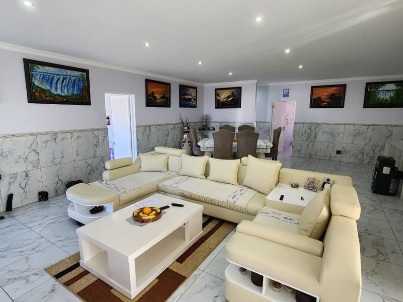 Spacious open-plan living and dining area featuring marble-effect wall and floor tiling, recessed downlighting, and integrated air conditioning.