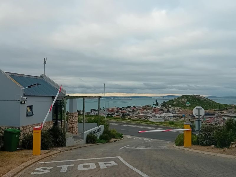 View of the residential estate entrance featuring a security boom gate, guard house, and paved driveway overlooking the surrounding coastal landscape.