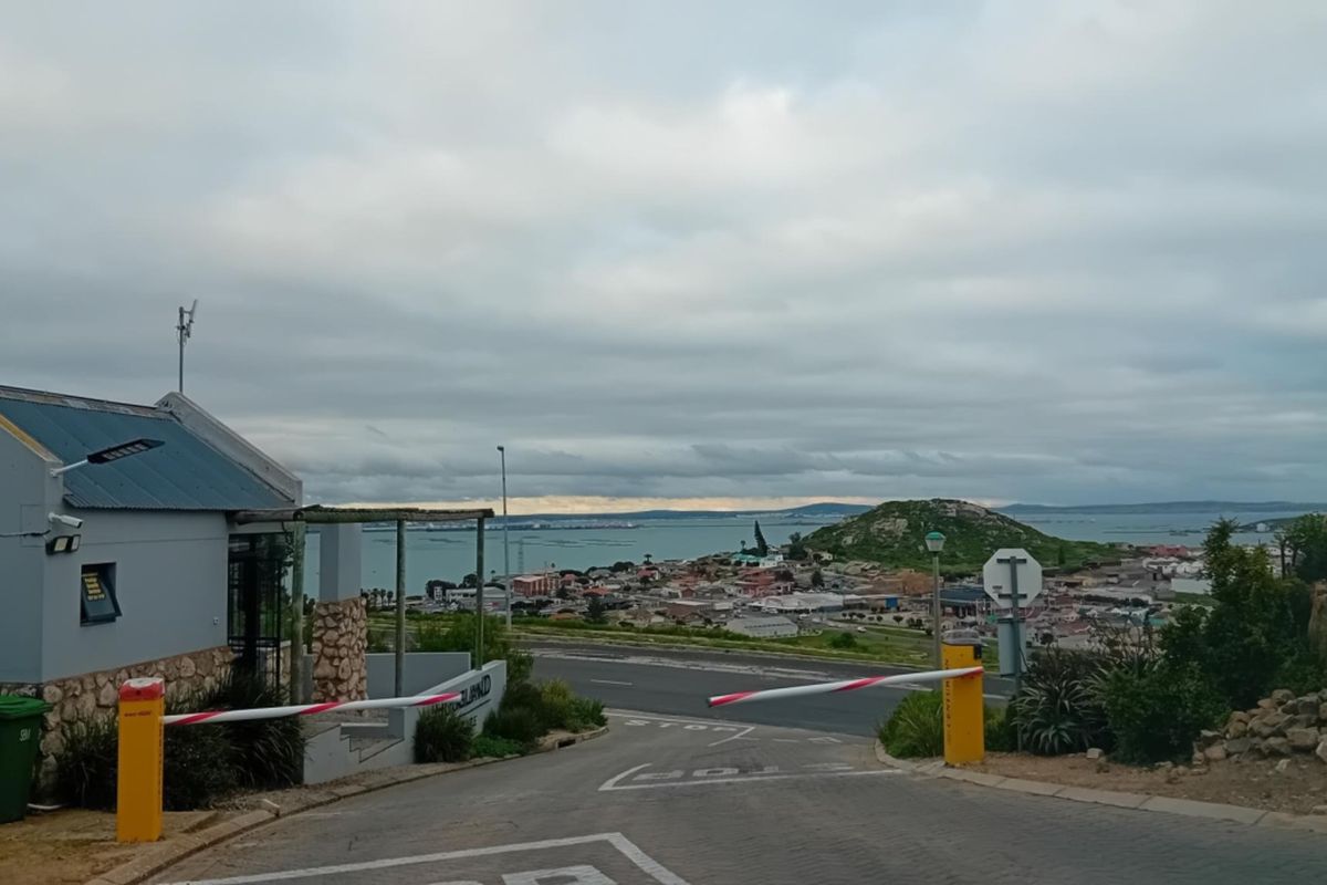 View of the residential estate entrance with a security boom gate, guard house, and panoramic coastal landscape in the background.