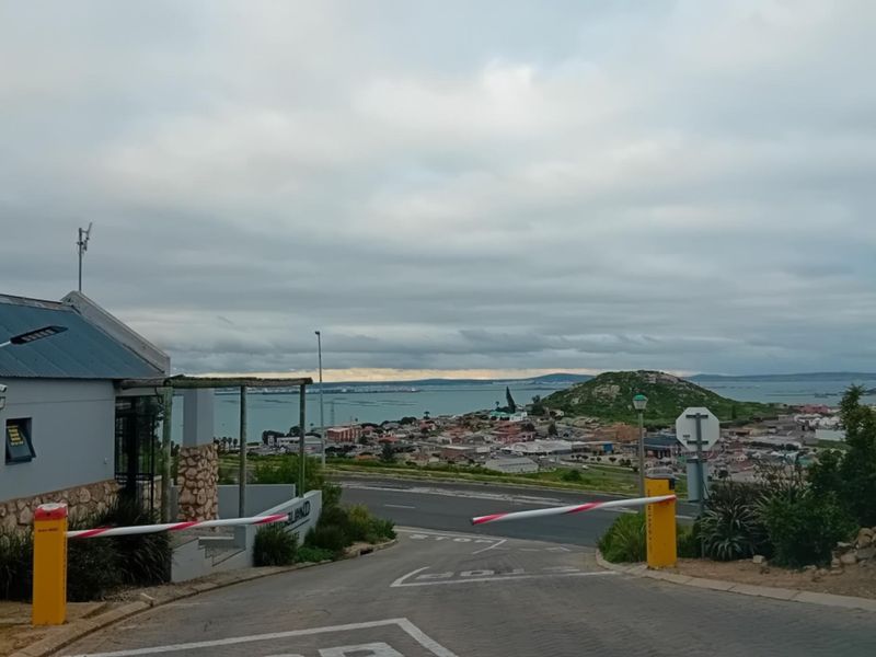 View of the residential estate entrance with a security boom gate, guard house, and panoramic coastal landscape in the background.