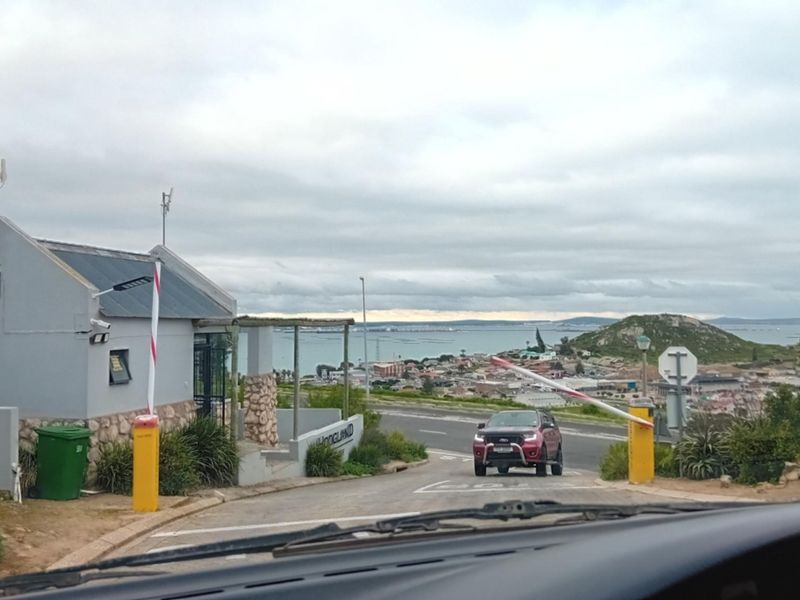 View of the residential estate entrance with a security boom gate, guard house, and surrounding coastal landscape.