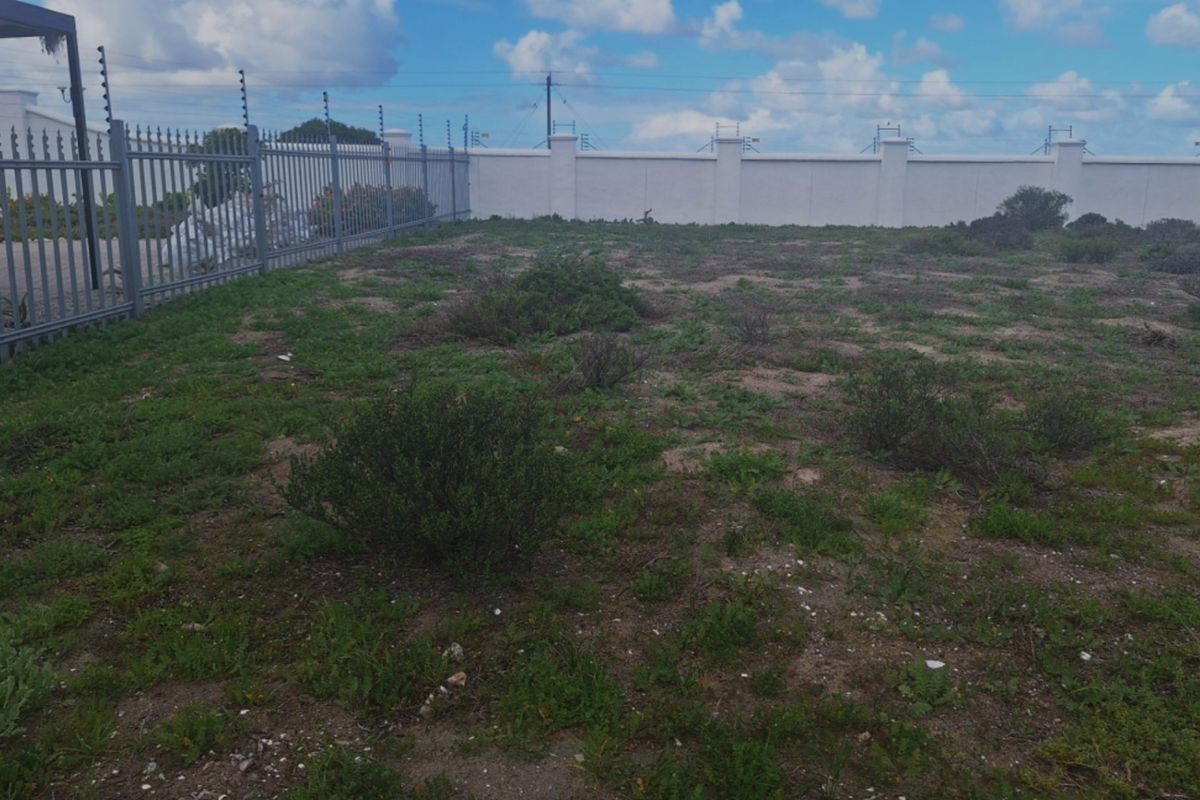 A vacant residential plot featuring a perimeter wall with electric fencing and a metal security gate.