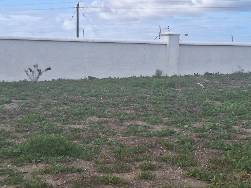 A vacant residential plot featuring a perimeter wall with installed electric fencing, providing a secure boundary for future development.