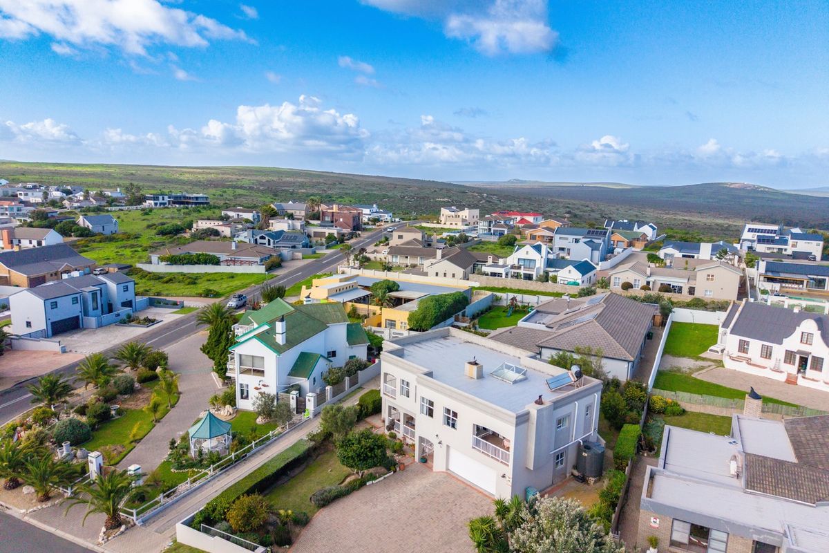 An elevated aerial view of a residential property featuring a paved driveway, garage, balcony, and solar water heating system within a suburban neighborhood.