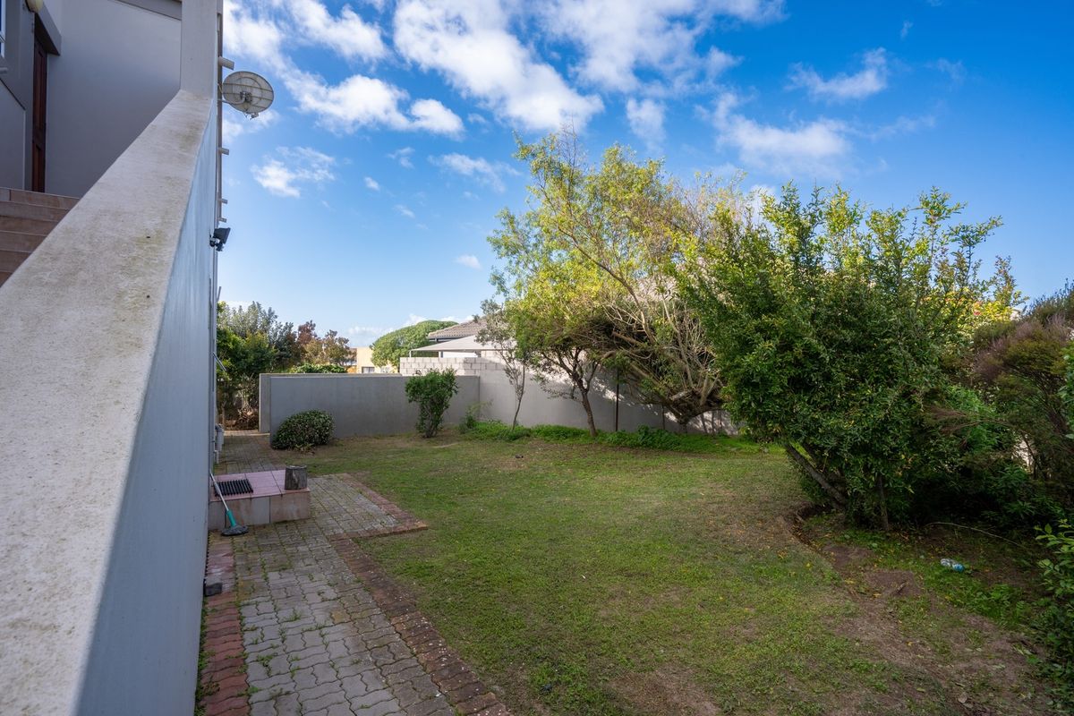 A rear garden area featuring a paved walkway, boundary wall, and established trees, providing a private outdoor space.