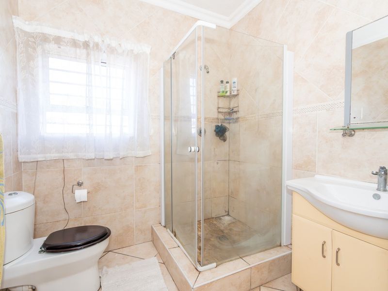 A functional bathroom featuring a glass shower enclosure, vanity cabinet with basin, and neutral wall and floor tiling.